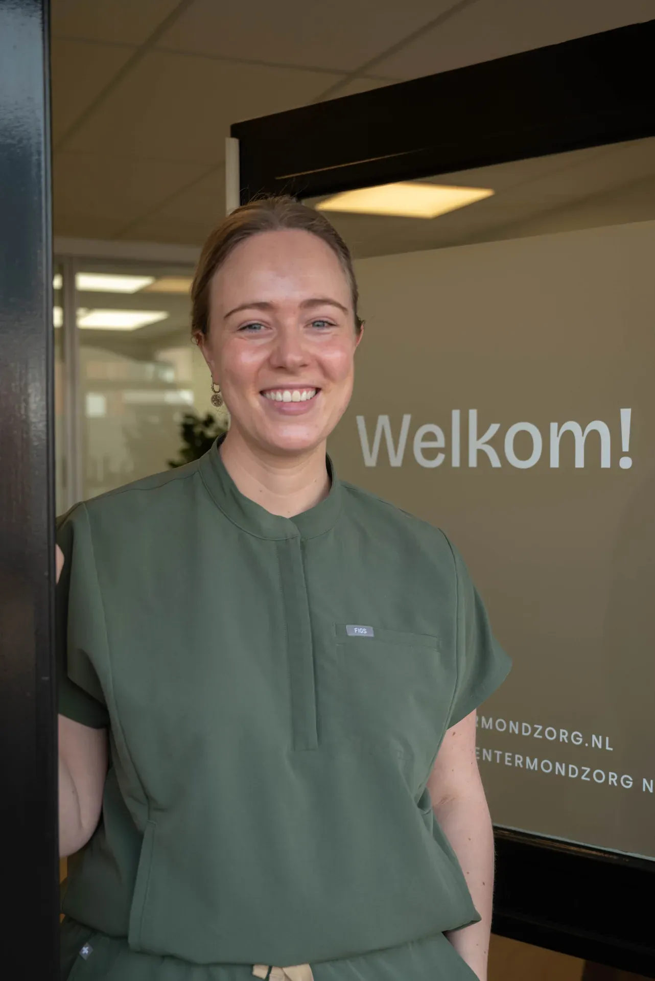 Portret van Jonne bij de ingang van de praktijk, met ‘Welkom!’ op het raam