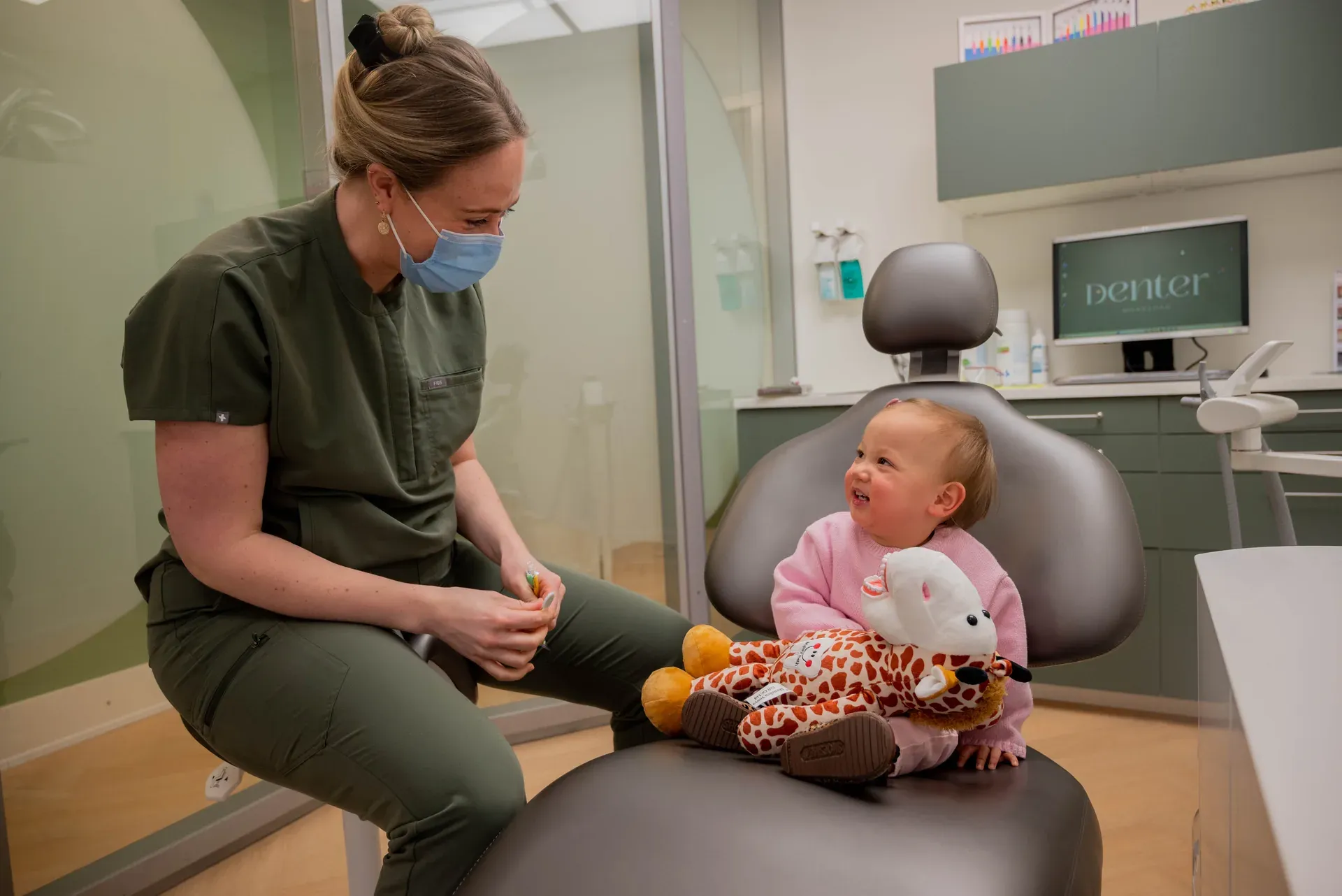 Peuter met knuffelgiraf in de behandelstoel bij haar eerste bezoek, met Jonne ernaast